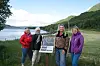 Fire kvinner står ved eit informasjonsskilt ved fjorden.