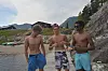 Tre menn står på ei steinstrand og held opp eit fiskereiskap.