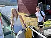 To ungdomar står ved ein båt ved ei brygge med raudt naust i bakgrunnen.