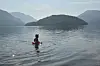 Person i vatn framfor fjord og fjell.