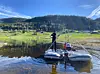 To personar på ei flåte ved vatnet i fjellandskap.