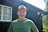 Mann i grøn T-skjorte framfor mørkt trehus.
