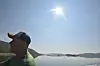 Mann i caps ser ut over fjord og fjell under sterk sol.
