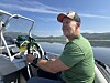 Mann ved roret i motorbåt på vatn.