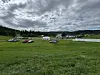 Parkerte bilar, telt og opne grasflater under skya himmel.