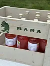 Treflasker med saft står i ei trekasse utandørs.