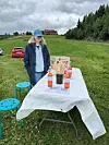 Kvinne står ved bord med flasker og måleriutstyr på grasbakke.