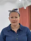 Kvinne i blå skjorte med hårband sit framfor lyse og raude tekstilar.