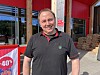 Mann står ved butikkinngang med raud rabattplakat og varer i hyller.