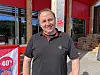 Mann står ved butikkinngang med raud rabattplakat og varer i hyller.