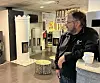 Ein mann står i eit rom med vedomn, trekubbe og plakatar.
