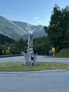 To personar står ved ei steinskulptur ved ein fjellveg.