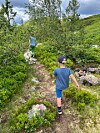 To barn går på ein smal sti i grønt fjellterreng.