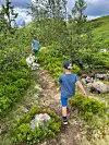 To barn går på ein smal sti i grønt fjellterreng.