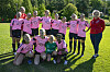 Fotballspelarar i rosa drakter posar på ein grasbane med trenaren ved sida.