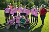Fotballspelarar i rosa drakter posar på ein grasbane med trenaren ved sida.