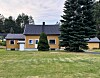 Gult hus med mørkt tak ved plen og graner.
