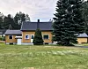 Gult hus med mørkt tak ved plen og graner.