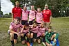 Eit fotballag i rosa drakter poserer på ei grasbane.