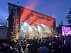 Publikum ser eit band spele på ei opplyst utandørsscene om kvelden.