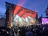 Publikum ser eit band spele på ei opplyst utandørsscene om kvelden.