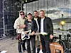 Fire musikarar står saman framfor instrument og scenelys utandørs.