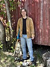 Person står ved raud trevegg ute og held ein lang stav.
