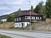 Mørkt hus i skråning ved veg, med skog og gatelys.