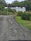 Grusveg som svingar mot eit hus i eit grønt landskap.