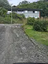 Grusveg som svingar mot eit hus i eit grønt landskap.