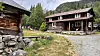 Tradisjonelle tømmerhus ved ein grusveg i eit grønt fjellandskap