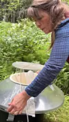 Kvinne arbeider med ein stor rund metallkonstruksjon mellom grøne plantar.