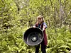 Kvinne held eit stort, rundt svart objekt framfor seg i ein skog.