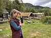 Kvinne skjermer augo på ein grasplen framfor eit trehus og fjell.