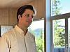Mann i lys skjorte står ved eit stort vindauge innandørs.