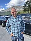 Mann i rutete skjorte står på ein parkeringsplass framfor eit fjell.