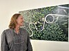 Kvinne står ved eit innramma kunstverk med grøne blad og kvit slyngform.