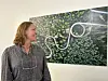 Kvinne står ved eit innramma kunstverk med grøne blad og kvit slyngform.