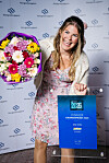 Kvinne med blomsterbukett og blått prisdiplom framfor ein NorgesGruppen-bakvegg.