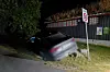 Mørk bil ved vegkanten, med parkeringsforbodsskilt og inngjerda bygg i bakgrunnen.