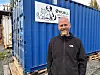 Mann i svart jakke står framfor ein blå container med ØYFJELL-skilt.