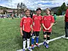 Tre unge fotballspelarar i raude drakter står saman på ei grasbana.