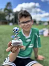 Ung fotballspelar held fram ein pokal på ei grasbane.