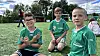 Tre unge fotballspelarar sit på graset i grøne drakter.