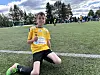 Ung fotballspelar i gul drakt sit på kne med ei drikkeflaske på kunstgraset.