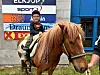 Barn sit på ein brun ponni ved ein butikkfasade.