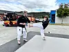 To personar øver på kampsport på matter framfor parkerte brannbilar.