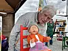 Kvinne bøyer seg over ei babydukke i ein raud stol ved ein marknadsstand.