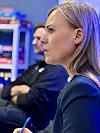 Kvinne i profil held ein blå penn medan ho sit i eit innandørs møte.