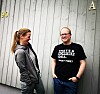 To personar står ved ein grå vegg, medan den eine ser på den andre.